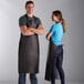 A man and woman wearing Choice brown vinyl aprons in a professional kitchen.