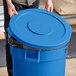 A person holding a Lavex blue commercial trash can lid.