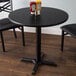 A black table with a Lancaster Table & Seating black table top and cross cast iron base plate.