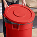 A person holding a Lavex red round commercial trash can lid.