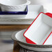 A white and red rectangular Tuxton China casserole dish with a black truffle band.