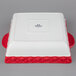 A white square Tuxton casserole dish with red trim and a black logo.