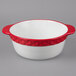 A white china casserole dish with red accents and handles.