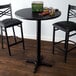 A Lancaster Table & Seating black bar table with a reversible cherry/black top on a cross cast iron base plate with two black stools.