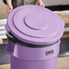 A woman opening a Lavex purple round commercial trash can lid.