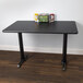 A black Lancaster Table & Seating table with a cherry/black reversible top and a black cast iron base.