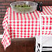 A white table with a red and white checkered vinyl table cover and a bowl of salad.