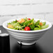 A Carlisle white melamine footed bowl filled with salad on a table.