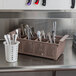 A brown Noble Products flatware rack on a counter with white containers of silverware.