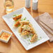 A rectangular white Acopa porcelain platter with dumplings and a glass of wine on it.