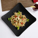 A black square Milano melamine plate with pasta and vegetables on a table