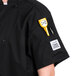 A black Chef Revival short sleeve chef jacket with yellow and black pens in the pocket.