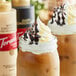 Two mason jars filled with coffee and topped with whipped cream next to a glass jar of Torani Puremade White Chocolate Flavoring Sauce.