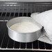 A person wearing gloves holding a Chicago Metallic round cake pan filled with white batter in an oven.