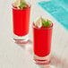 Two Acopa shooter glasses filled with red liquid and garnished with lime.