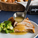 A plate of food with a Wavy Stainless Steel Ladle serving broccoli and chicken with gravy.