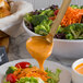 A ladle with hammered gold design pouring orange sauce over a bowl of salad.