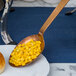 A vintage slotted spoon with a hammered bronze handle serving corn on a plate.