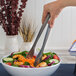 A person using American Metalcraft hammered stainless steel tongs to serve a salad.