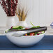 A bowl of salad with American Metalcraft wavy stainless steel tongs on a table.