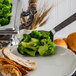 An American Metalcraft stainless steel slotted spoon serving broccoli on a plate.