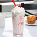 A Libbey jumbo paneled drinking glass filled with a milkshake topped with whipped cream and a cherry.