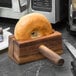 A bagel being sliced by a Fox Run wood bagel slicer with handle.