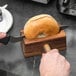 A person using a Fox Run wood bagel slicer to cut a bagel.