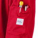 A red Mercer Culinary Millennia Air long sleeve cook jacket with a white label over the pocket holding a yellow pen.