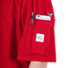 A person wearing a red Mercer Culinary cook jacket with a full mesh back, pocket, phone, and pen.