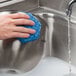 A hand holding a blue Scotch-Brite Low Scratch Scour Pad over a stainless steel sink.