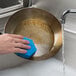 A hand using a blue Scotch-Brite Low Scratch Scour Pad to wash a pan.