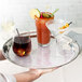 A hand holding a Thunder Group stainless steel serving tray with drinks including a brown glass jar and a martini glass.