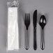 A white plastic bag with a black handle containing a pre-rolled Hoffmaster Linen-Like white napkin with black heavy weight plastic cutlery.