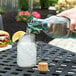 A hand pouring water from a Tablecraft green glass bottle with a cork into a glass on a table with a lemon slice and ice.