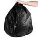 A person's hand holding a Berry black low density trash bag.