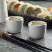 A Tuxton white porcelain sake cup filled with liquid on a table with chopsticks.