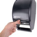 A hand pressing a button on a San Jamar Duett Classic toilet tissue dispenser in black.