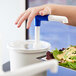 A hand using a white and blue pump to dispense salad from a clear plastic container.