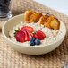 A Tuxton matte beige china bowl filled with oatmeal topped with strawberries and blueberries.