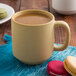 A close up of a Tuxton matte beige mug filled with coffee on a table with macarons.