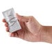 A hand holding a small white packet of Dial White Marble Breck Conditioner.