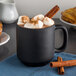 A Tuxton TuxTrendz matte black china mug filled with hot chocolate with marshmallows and cinnamon sticks.
