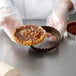 A person in gloves holding a tart in a Gobel fluted tart pan.