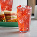 A clear GET Bahama plastic tumbler filled with red liquid and ice on a table with a sandwich.