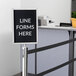 A Lancaster Table & Seating stainless steel stanchion sign frame with a sign that says "Line Forms Here" on a pole.