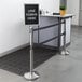 A Lancaster Table & Seating stainless steel stanchion with a black and white sign on top.