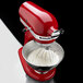 A red KitchenAid stand mixer with a stainless steel mixing bowl of whipped cream.