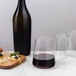 A bottle of red wine and a Stolzle stemless wine glass filled with wine on a table with food.