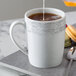A white Schonwald porcelain mug with a grey liquid being poured into it.